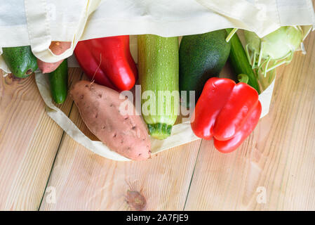 Welt frei von Kunststoff. Wiederverwendbare umweltfreundliche Leinwand einkaufen Tasche mit Gemüse - süsse Kartoffeln, Zucchini, Paprika, Tomaten, Gurke und Avocado auf hölzernen Schreibtisch. Organische Produkte. Weniger Kunststoff. Stockfoto