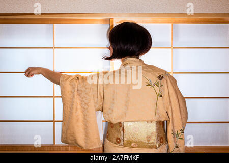 Traditionelle japanische Haus Schiebetür Fenster mit Frau in Schwarz Haar im Kimono Kostüm stehen mit ausgestreckten Hand mit Hülse Stockfoto