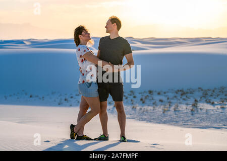 Frau und Mann Paar stehend auf Sand Hill in White Sands Dunes National Monument in New Mexico mit Sonnenuntergang liebevoll an einander umarmen suchen Stockfoto