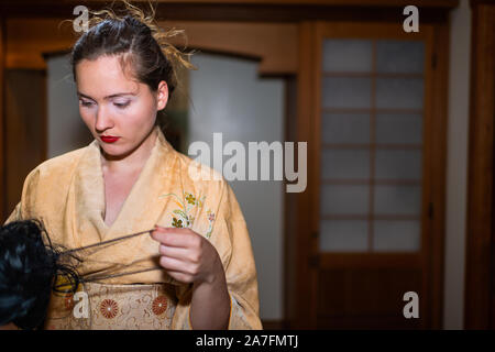 Junge Frau im Kimono fertig, durch traditionelle hölzerne Tür Holding schwarze Perücke in japanischen Haus home Stockfoto