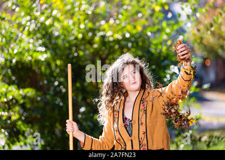 Junge Frau in Yard Hinterhof harken Sammeln von trockenen Herbst Laub Eichenlaub ständigen Holding Laub fällt mit Rechen im sonnigen Herbst Stockfoto