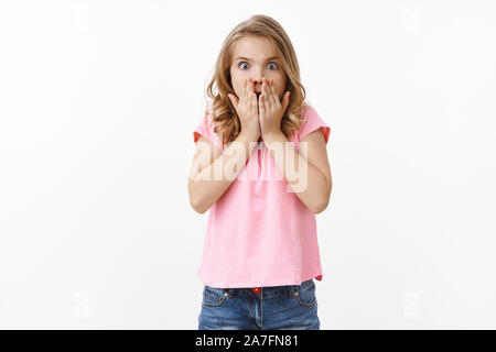 Sprachlos cute blonde Mädchen, Jugend-kid nach Luft schnappend, Deckel Mund mit Palmen von Erstaunen und Aufregung überrascht, starren Kamera beeindruckt, überrascht Stockfoto