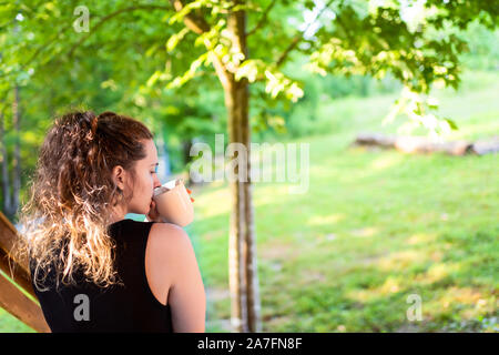 Spring House Veranda mit Frau sitzt auf der Treppe des Hauses in der vorderen oder hinteren Hof morgen Blockhaus Cottage trinken Kaffee oder Tee Stockfoto