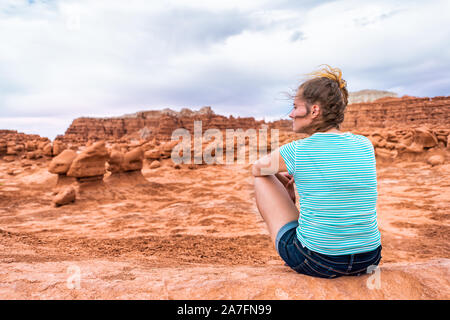 Frau Wanderer zurück sitzen auf hoodoo Sandstein Felsformationen mit bewölkt Sturm Himmel und wind Wüstenlandschaft im Goblin Valley State Park in Ut Stockfoto