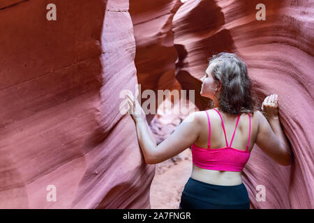 Rückseite der jungen Frau zu Fuß auf Wanderung berühren Formationen Wellenformen auf engen Antelope Slot Canyon in Arizona im Sommer mit Sport-BH Stockfoto