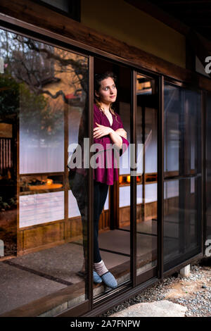 Junge Kälte zitternden Frau in Japan suchen durch offene Fenster Schiebetür indoor auf traditionellen Japanischen Garten mit Kies Stein Felsen in Stockfoto