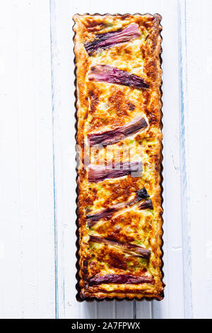 Gesalzener Kuchen mit Frühlingszwiebeln gestreift, mit Fontina, Eier, Sahne, und Würstchen, Violett stripses oben, rechteckigen Formen auf einem dunklen Hintergrund Stockfoto