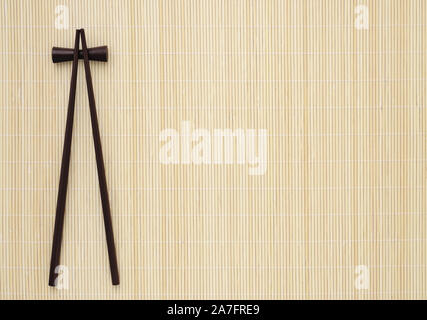 Bambus Matte mit zwei dunkelbraune Sushi mit Stäbchen. Menü Hintergrund. Stockfoto