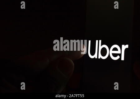 Uber Logo auf einem Bildschirm des Smartphones in einem dunklen Raum und einen Finger zu berühren. Stockfoto