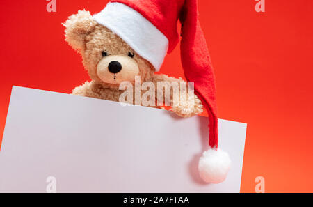 Weihnachten Karte Vorlage. Teddybär mit weihnachtsmütze Holding eine leere Karte, rote Farbe Hintergrund Kopie Raum Stockfoto