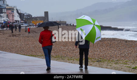 Lyme Regis, Dorset, Großbritannien. 2. November 2019: UK Wetter: Ein Paar bietet Schutz unter Sonnenschirmen, wenn sie entlang der Küste spazieren, während schwere Regenfälle die beliebte Küstenstadt an nassen und regnerischen Nachmittagen übertatteln. Quelle: DWR/Alamy Live News. Stockfoto