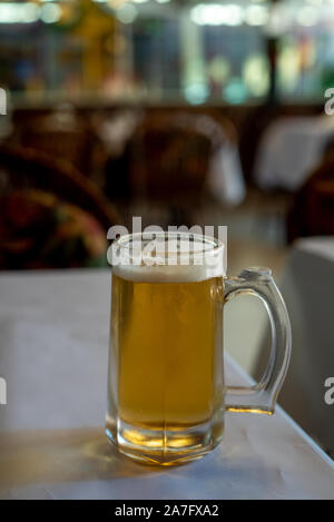 Ein Glas Bier von der Seite in einem in einem Restaurant gesehen, über eine Tabelle mit weißen Tischtüchern bedeckt, selektiver Fokus, Glas ist voll Stockfoto