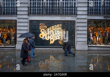 2. November 2019. Superdry store Fenster mit gold Schriftzug auf nasser Fahrbahn im Herbst Wetter widerspiegelt, der Regent Street London, UK. Stockfoto