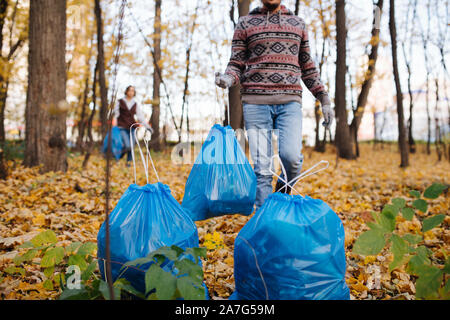 Menschen Kunststoff blau Abfallbeutel zu einem Stapel in einen saisonalen Wald im Herbst. Stockfoto