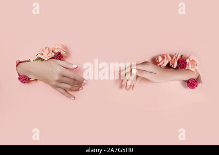 Legen Sie die Hände mit künstlichen Blumen aus Loch rosa Papier Hintergrund. Hand in verschiedenen Posen, das Muster layout für Ihre Collage. Kosmetik ha Stockfoto