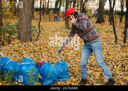 Mann neben der Papierkorb in einem Wald arrangieren Müllabfuhr am Telefon zu stapeln. Stockfoto