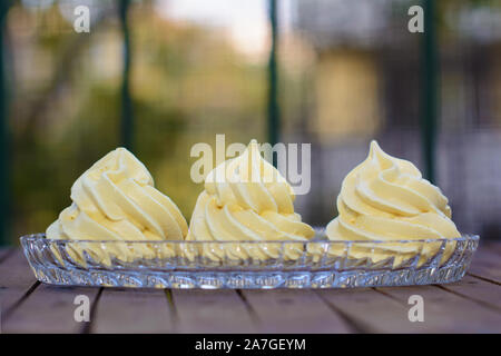 Drei gelbliche Baisers in einem Glas Kuchen Platte Stockfoto