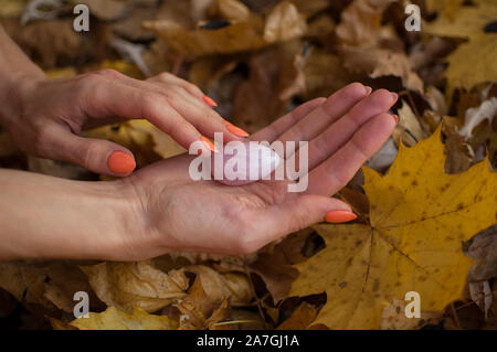 Weibliche hand mit orange Maniküre Holding rosa Quarz yoni Ei für vumfit, imbuilding oder Meditation auf gelbem Hintergrund Laub im Herbst Stockfoto