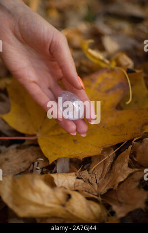 Weibliche hand mit orange Maniküre Holding transparent violett Amethyst yoni Ei für vumfit, imbuilding oder Meditation auf gelbem Laub Hintergrund Stockfoto