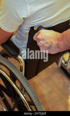 Detail eines Menschen Hand drücken einen Rollstuhl mit einem Patienten. Behinderung Konzept Stockfoto