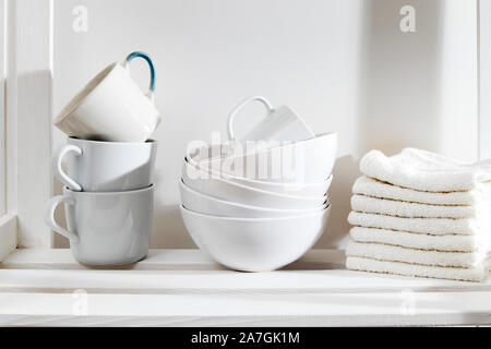 Storage System in der Küche. Vitrinen mit weißen Tassen, Schüsseln und Handtücher. Weiß auf Weiß Stockfoto