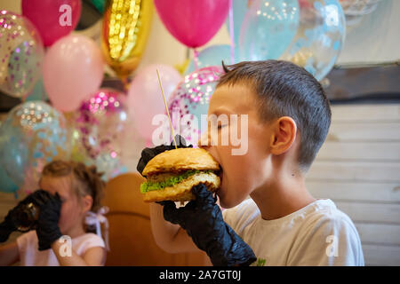 Der stattliche kleine Junge Burger essen in schwarzem Gummi Handschuhe. Stockfoto