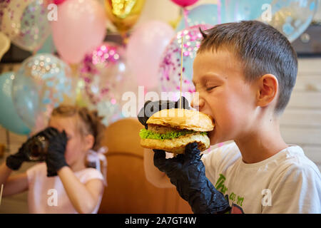 Der stattliche kleine Junge Burger essen in schwarzem Gummi Handschuhe. Stockfoto