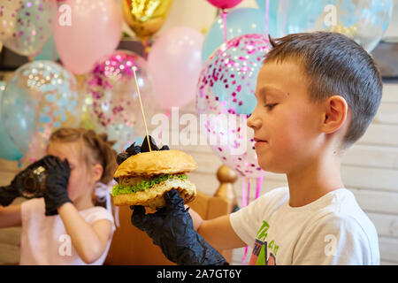 Der stattliche kleine Junge Burger essen in schwarzem Gummi Handschuhe. Stockfoto