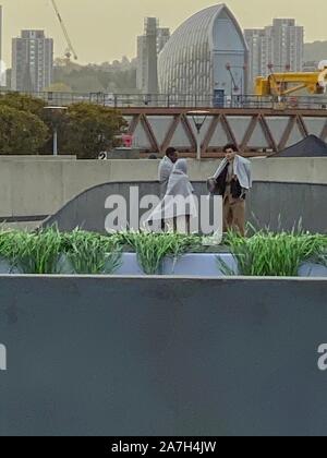 Silvertown, London, UK. 2. November 2019. Akteure warten an den Dreharbeiten zu Szene in Schöne neue Welt zu nehmen, ein Netflix 8 Teil der Serie veröffentlicht im November 2020. Thames Barrier im Hintergrund. Stockfoto