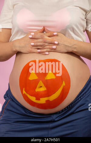 Junge schwangere Frau mit Kürbis Halloween auf dem Bauch Closeup Portrait gemalt Stockfoto