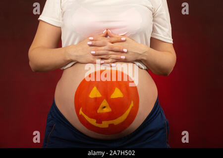 Junge schwangere Frau mit Kürbis Halloween auf dem Bauch Closeup Portrait gemalt Stockfoto