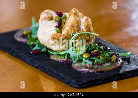 Baked Brie in einem Blätterteig gefüllt mit Früchten der Saison und Grüns serviert. Stockfoto