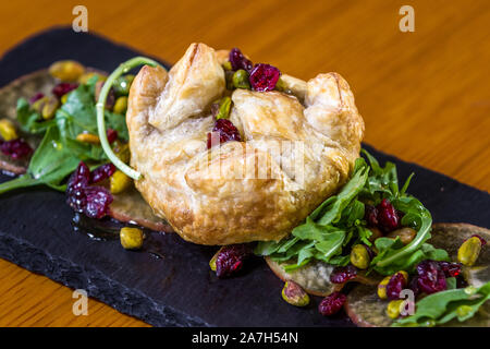 Baked Brie in einem Blätterteig gefüllt mit Früchten der Saison und Grüns serviert. Stockfoto