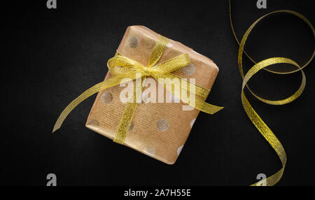 Geschenkbox in Handwerk Papier mit Goldband auf schwarzem Hintergrund gewickelt. Weihnachten Konzept. Kopieren Sie Raum, Overhead Stockfoto