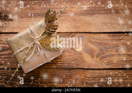 Geschenkbox in Handwerk Papier mit goldenen Tanne und Kegel auf rustikalen Holzmöbeln Hintergrund gewickelt. Weihnachten Konzept. Kopieren Sie Raum, Overhead Stockfoto