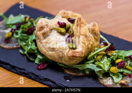 Baked Brie in einem Blätterteig gefüllt mit Früchten der Saison und Grüns serviert. Stockfoto