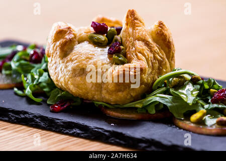 Baked Brie in einem Blätterteig gefüllt mit Früchten der Saison und Grüns serviert. Stockfoto