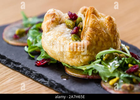 Baked Brie in einem Blätterteig gefüllt mit Früchten der Saison und Grüns serviert. Stockfoto