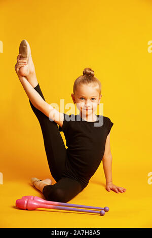 Mädchen gymnast Züge mit Gymnastik Vereine auf gelben Hintergrund. professionelle Kinder- Sport. Schöne jugendlich Mädchen tun, rhythmische Gymnastik Übungen Stockfoto