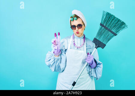 Putzfrau Spaß. Ältere Menschen lustig Hausfrau um Narren mit einem Besen. Voller Körper isoliert Blau. Komisch Putzfrau, alte Frau funky Stockfoto