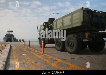 Us-Marines mit 12 Marine Regiment, 3rd Marine Division, die Vorbereitung auf ein High Mobility Artillery Rocket System Last auf die US-Armee Schiff Harpers Ferry (LCU-2022) Bei einer gemeinsamen Service HIMARS Einschiffung Training übung in Kin, Okinawa, Japan, Okt. 31, 2019. Dieses Ereignis markiert das erste Mal ein Marine HIMARS auf eine Armee Landing Craft im Indopazifik geladen wurde. Strategische Mobilität ist der Schlüssel im Indopazifik und die Fähigkeit, die HIMARS über Wasser zu transportieren ist eine wichtige Funktion, die die 3. Marine Division nun in der Lage ist, auf die sich die Partnerschaft mit der 10 Support Gruppe zu erweitern. (U.S. Stockfoto