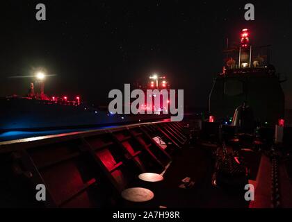 191029-N-PC 620-0239 Arabische Meer (Okt. 2010) 29, 2019) Die geführte-missile Cruiser USS Normandie (CG60) führt eine Auffüllung auf See mit der Royal Fleet auxiliary schnelle Flotte Tanker RFA Wave Ritter (A 389) in der Nacht. Die Normandie ist Teil der Ostküste Oberfläche Action Group und arbeitet in den USA 5 Flotte Bereich für Maßnahmen zur Erhöhung der Marineoperationen maritime Stabilität und Sicherheit in der Region zu gewährleisten und verbindet das Mittelmeer und den Pazifischen Raum durch den Westlichen Indischen Ozean und drei strategischen Punkten ersticken. (U.S. Marine Foto von Mass Communication Specialist 2. Klasse Michael H. L Stockfoto