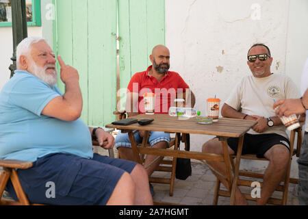 Skiathos Griechenland - 4. August 2019; drei Männer an ihren regelmäßigen Treffpunkt in der Griechischen Insel Dorfstraße für Morgen trinken, Klatsch und Tratsch. Stockfoto