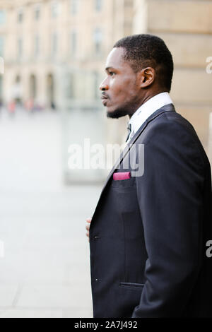 Portrait von afro-amerikanische glücklich Mann mit dunklen Anzug und stehen in der Nähe der Gebäude. Stockfoto