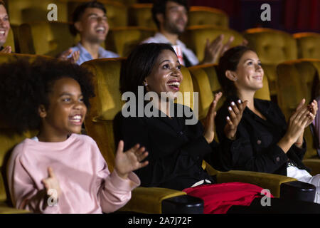 Schwarze Frau und Mädchen, das Publikum bei Laune und Händeklatschen beim Sitzen inmitten der Leute nach dem Film im Kino begeistert Stockfoto