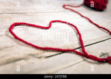 Rote wollene Ball und String auf Holz- Hintergrund, Symbol Herz Stockfoto