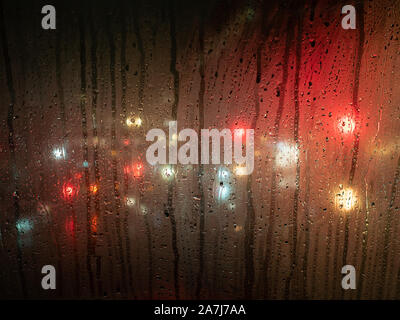 Regentropfen auf einem Bus-Fenster mit unscharfen Scheinwerfer hinter Stockfoto
