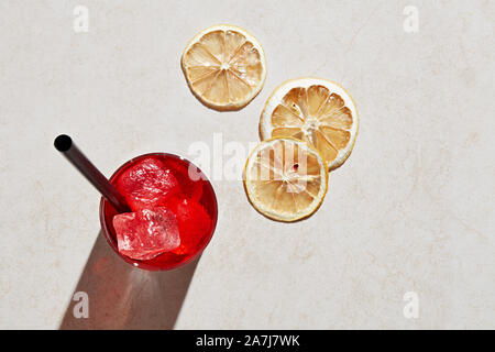 Glas Erfrischende Sommer Cocktail mit Eis, Stroh und trockene Zitronenscheiben auf weißen Stein Oberfläche. Ansicht von oben mit harten Sommer Sonnenlicht. Stockfoto