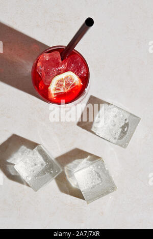 Glas Erfrischende Sommer Cocktail trinken mit Zitrone, Stroh und Eiswürfel auf weißen Stein Oberfläche. Ansicht von oben mit harten Sommer Sonnenlicht. Stockfoto