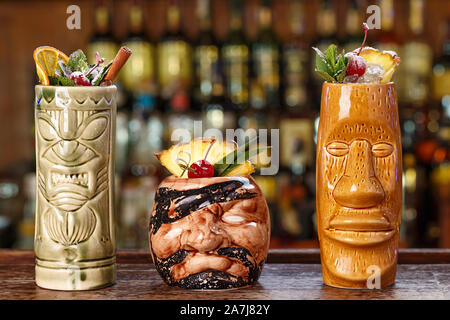 Satz von drei tropische Cocktails in Tiki Gläser in einem Nachtclub auf dem Hintergrund einer Theke. Lange alkoholische Cocktails mit Eis, Rum und verschiedene Stockfoto